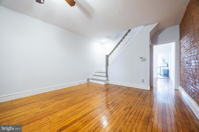 unfurnished living room featuring a ceiling fan, baseboards, brick wall, stairs, and hardwood / wood-style flooring