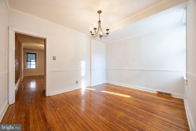 empty room with visible vents, an inviting chandelier, crown molding, and hardwood / wood-style flooring