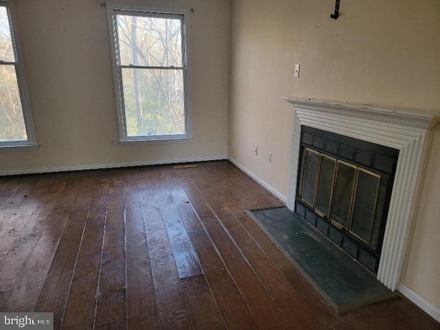 unfurnished living room featuring a glass covered fireplace, dark wood-type flooring, and baseboards