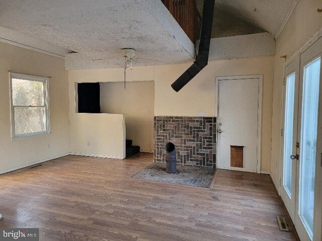 unfurnished living room featuring visible vents, ornamental molding, a textured ceiling, wood finished floors, and lofted ceiling