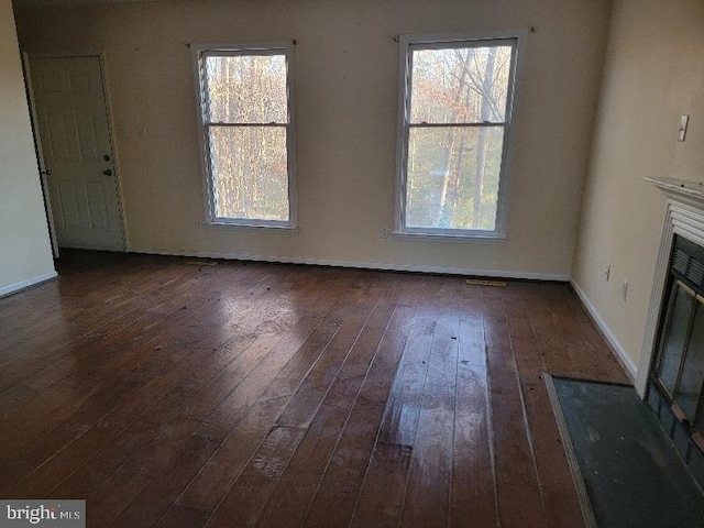 unfurnished living room with a fireplace with flush hearth, a healthy amount of sunlight, baseboards, and wood-type flooring