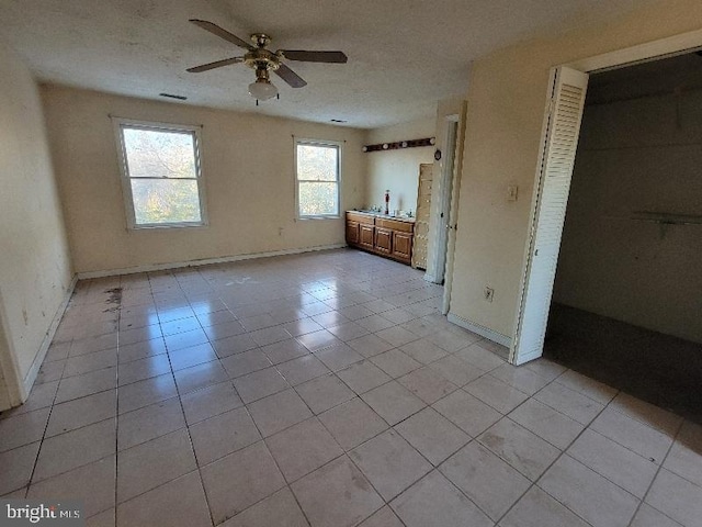 unfurnished bedroom with visible vents, a ceiling fan, a textured ceiling, light tile patterned flooring, and baseboards