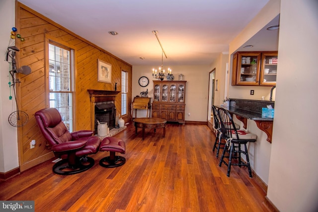 living room with baseboards, wood walls, a fireplace, an inviting chandelier, and wood finished floors