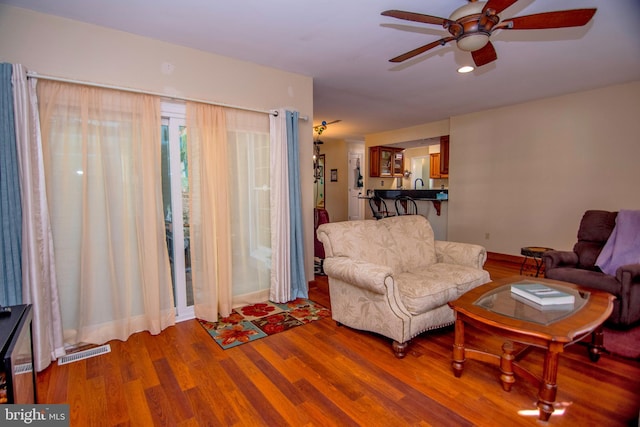 living area featuring a ceiling fan, wood finished floors, visible vents, and baseboards