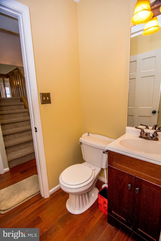 half bathroom featuring toilet, vanity, baseboards, and wood finished floors