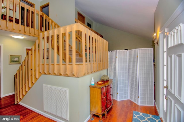 staircase featuring vaulted ceiling, visible vents, baseboards, and wood finished floors