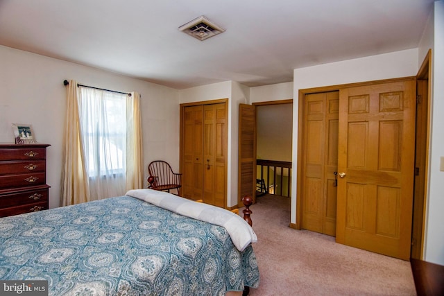 bedroom featuring visible vents, light colored carpet, and multiple closets