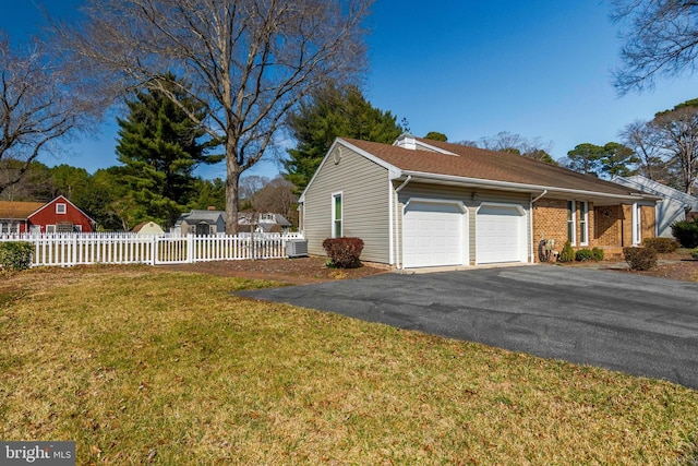 view of side of home featuring brick siding, fence, a yard, a garage, and driveway