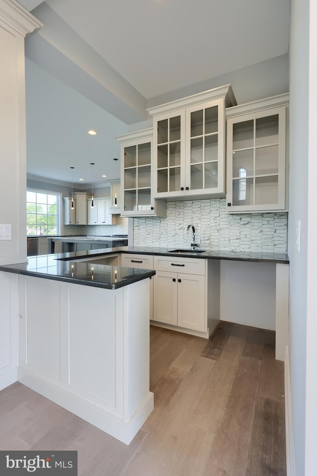 kitchen with light wood finished floors, dark countertops, a peninsula, a sink, and backsplash