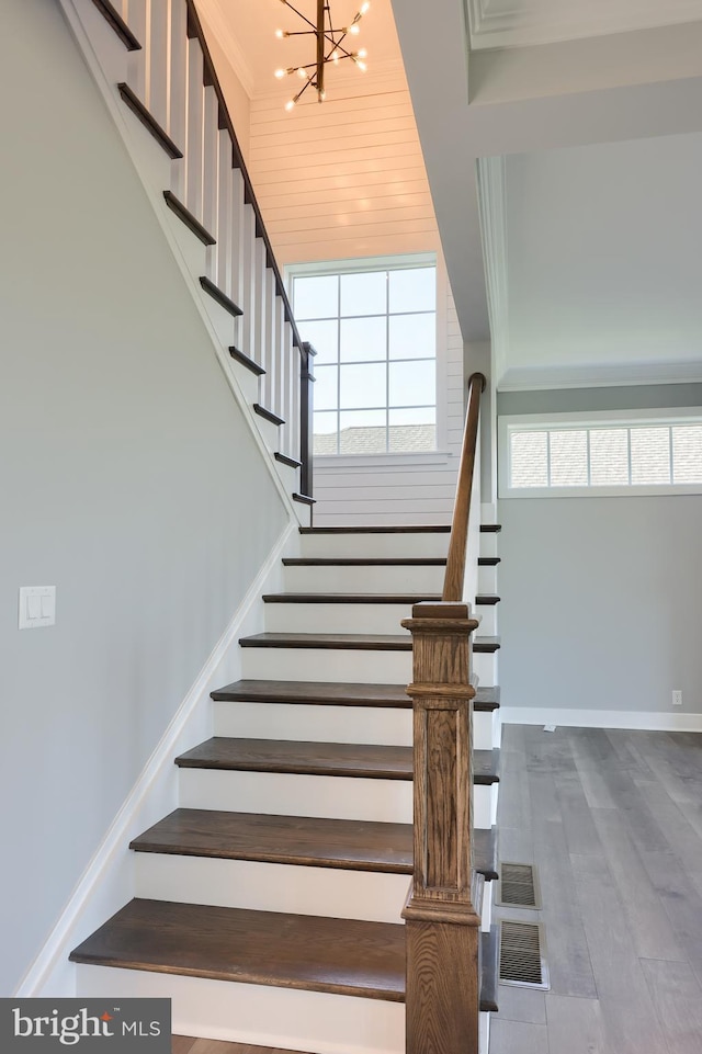 stairs featuring crown molding, visible vents, wood finished floors, a chandelier, and baseboards