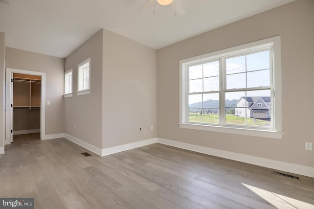 unfurnished bedroom with baseboards, a spacious closet, visible vents, and wood finished floors