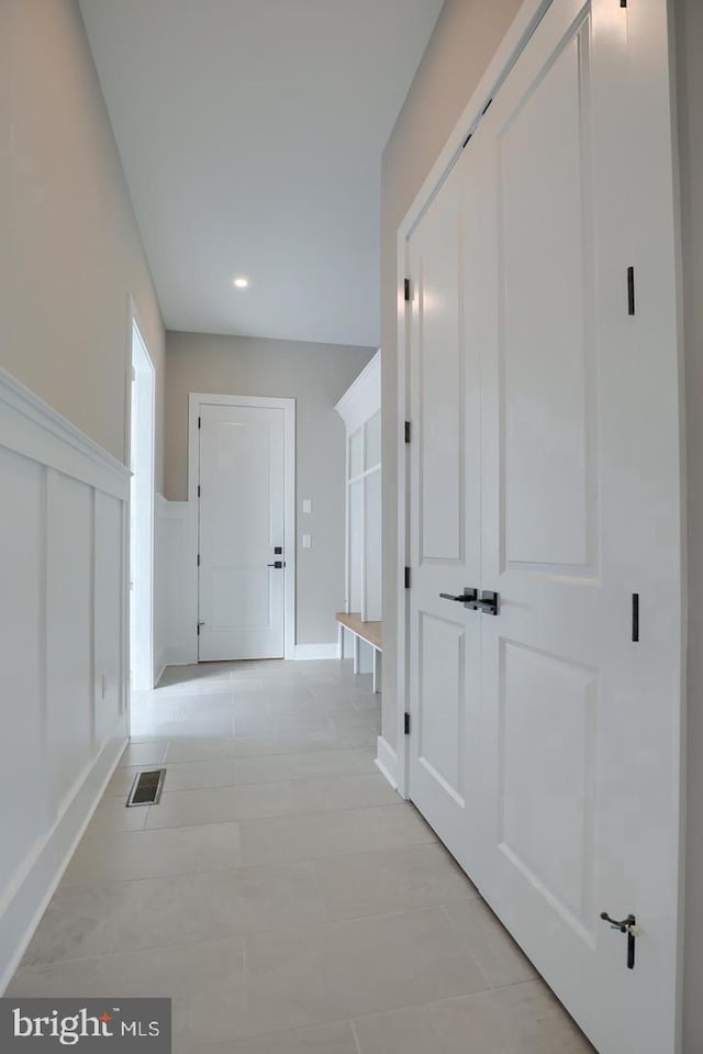 corridor with light tile patterned floors, visible vents, a decorative wall, and wainscoting