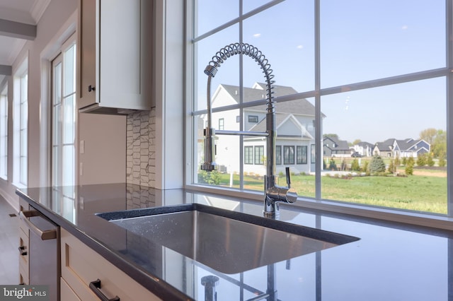 kitchen with a sink, white cabinetry, stainless steel dishwasher, a residential view, and dark stone counters