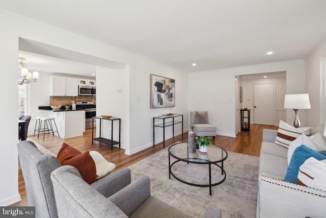 living room featuring crown molding, baseboards, recessed lighting, light wood-style floors, and a notable chandelier