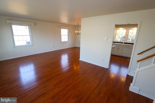 unfurnished room with a sink, dark wood-style floors, stairway, an inviting chandelier, and baseboards