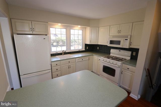 kitchen with backsplash, white appliances, white cabinetry, and a sink