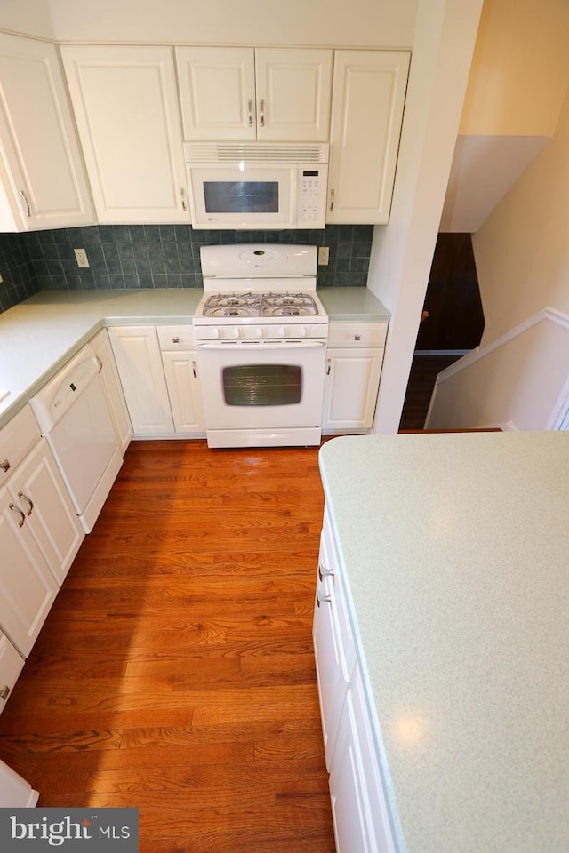 kitchen with tasteful backsplash, light countertops, wood finished floors, white appliances, and white cabinetry