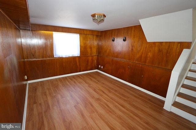 empty room with stairway, wood finished floors, baseboards, and wood walls