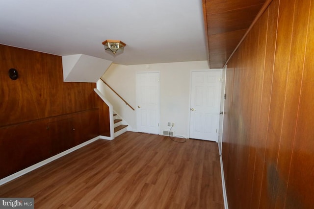 below grade area featuring stairway, wooden walls, visible vents, and wood finished floors