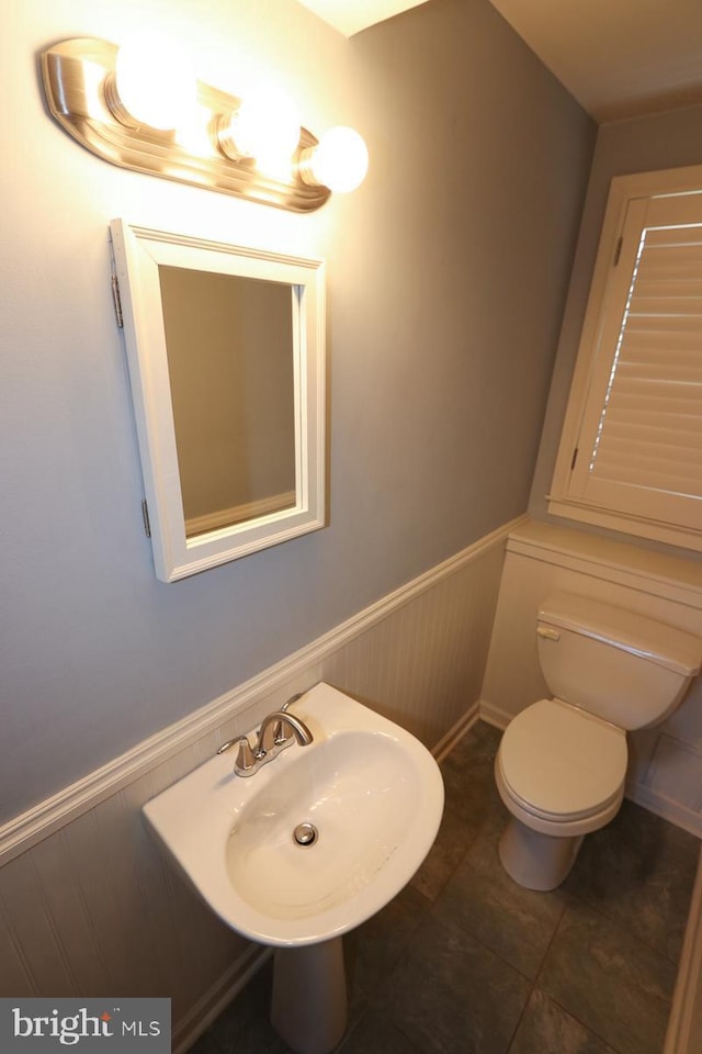 half bath with tile patterned flooring, wainscoting, and toilet