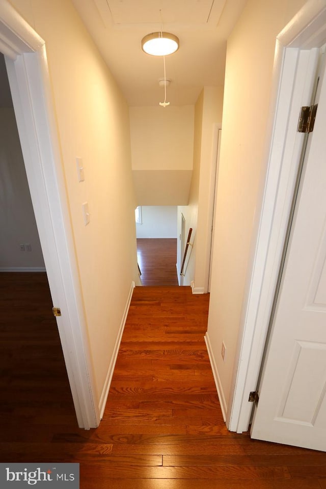 corridor featuring an upstairs landing, attic access, baseboards, and wood finished floors