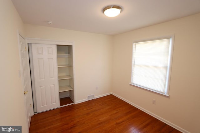 unfurnished bedroom with wood finished floors, visible vents, a closet, and baseboards