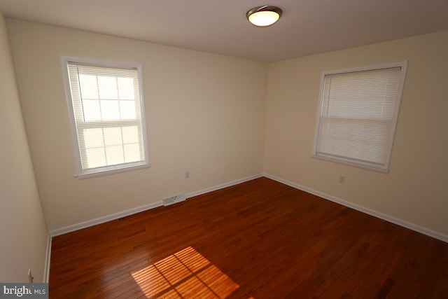 spare room with visible vents, baseboards, and dark wood-style flooring