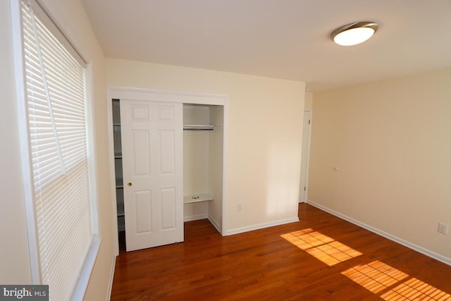 unfurnished bedroom featuring wood finished floors, baseboards, and a closet