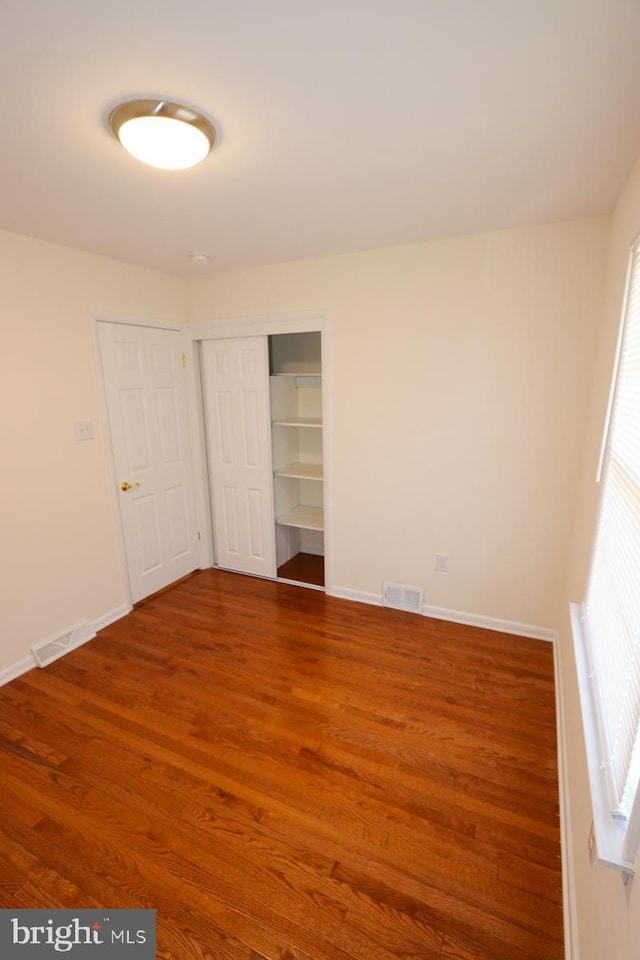 unfurnished bedroom with visible vents, baseboards, a closet, and wood finished floors