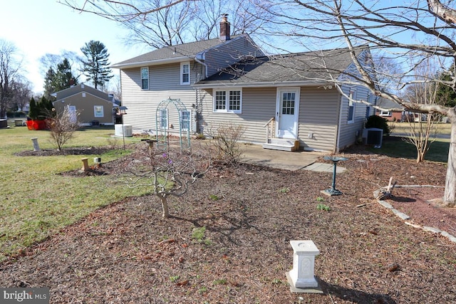 rear view of property with central air condition unit, a lawn, entry steps, and a chimney