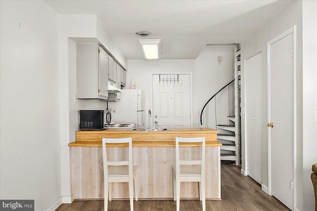 kitchen with wooden counters, a peninsula, dark wood finished floors, and freestanding refrigerator