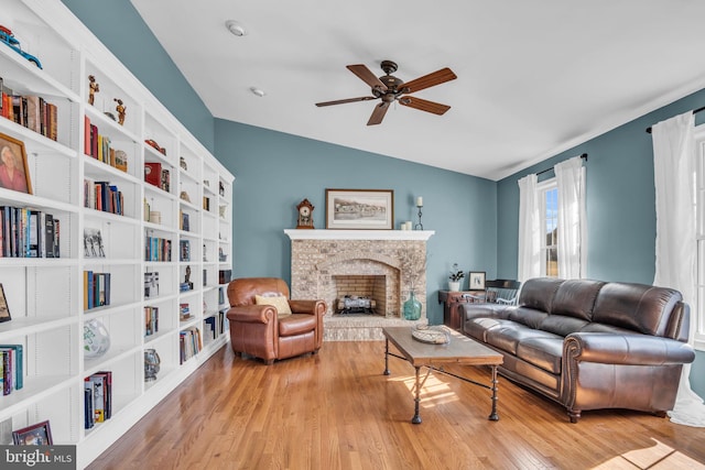 living room with a ceiling fan, vaulted ceiling, wood finished floors, and a fireplace with raised hearth