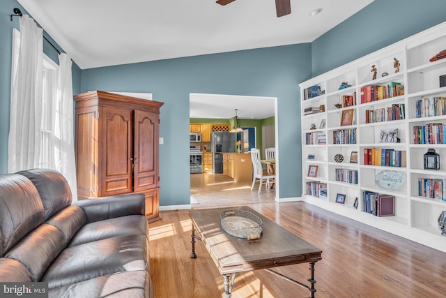 living area with baseboards, ceiling fan, built in features, lofted ceiling, and light wood-style flooring