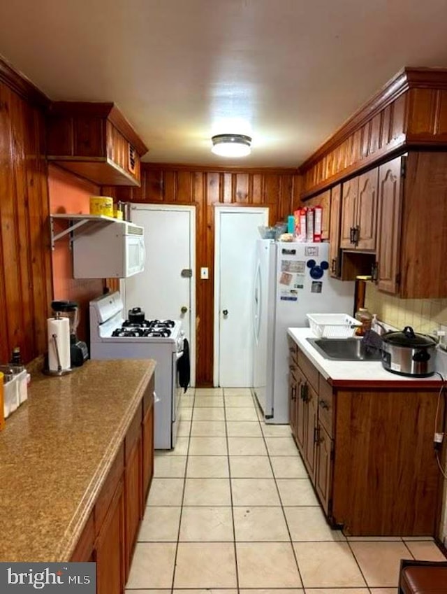 kitchen featuring light tile patterned flooring, white appliances, a sink, brown cabinets, and tasteful backsplash