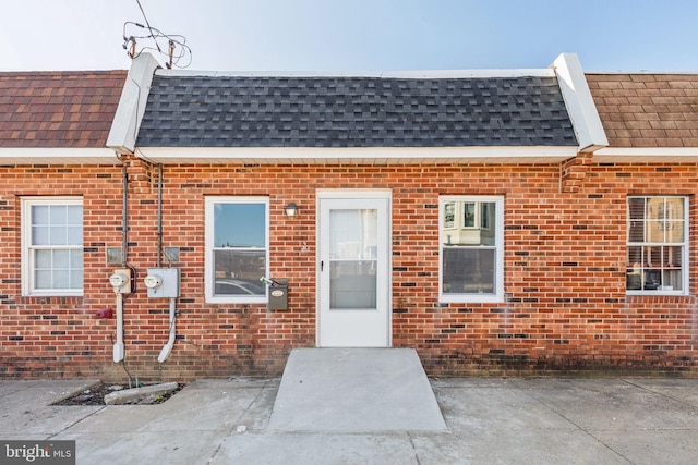 property entrance featuring mansard roof, brick siding, and roof with shingles