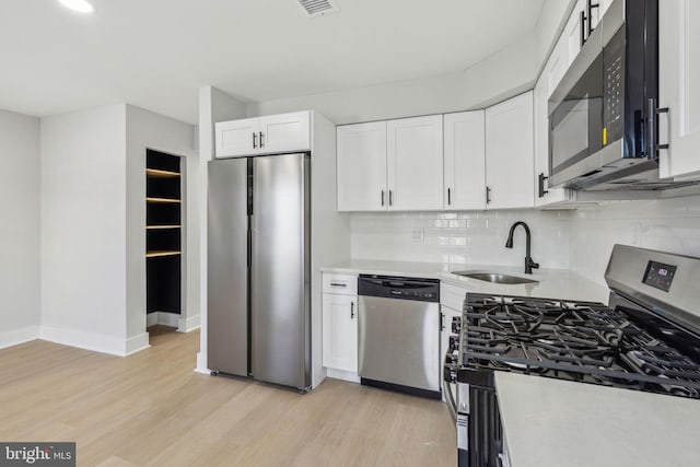 kitchen featuring light wood finished floors, a sink, stainless steel appliances, light countertops, and white cabinets