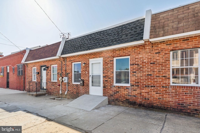 view of front facade with mansard roof, brick siding, and roof with shingles