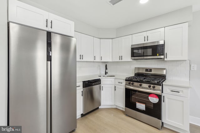 kitchen with a sink, tasteful backsplash, appliances with stainless steel finishes, white cabinets, and light countertops