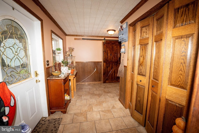 hallway with a wainscoted wall, an ornate ceiling, a barn door, wooden walls, and crown molding