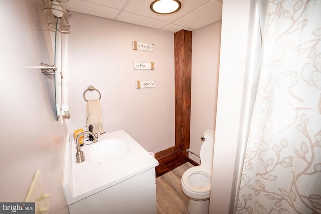 bathroom featuring a paneled ceiling, toilet, wood finished floors, and vanity