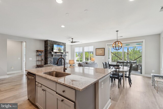kitchen with a stone fireplace, light wood-type flooring, dishwasher, a sink, and open floor plan