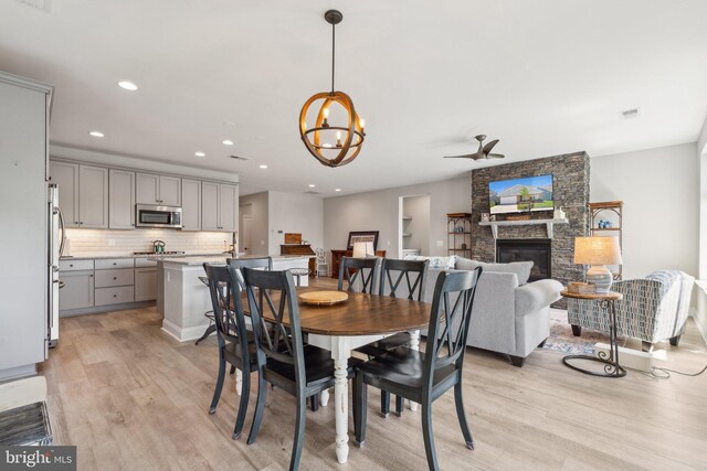 dining room featuring visible vents, light wood-style floors, a stone fireplace, recessed lighting, and ceiling fan with notable chandelier