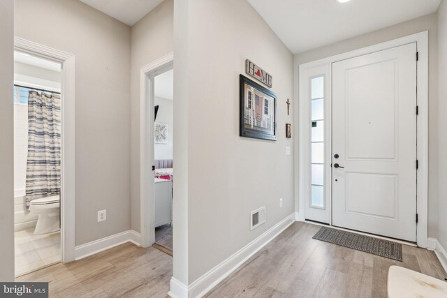 foyer entrance with light wood-type flooring, baseboards, and visible vents