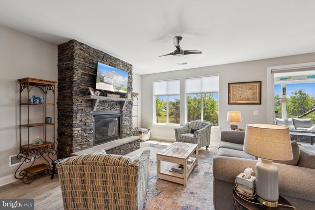 living area featuring a ceiling fan, baseboards, a stone fireplace, and wood finished floors