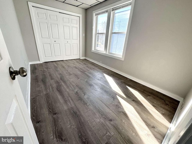 unfurnished bedroom featuring dark wood-type flooring, a closet, a paneled ceiling, and baseboards