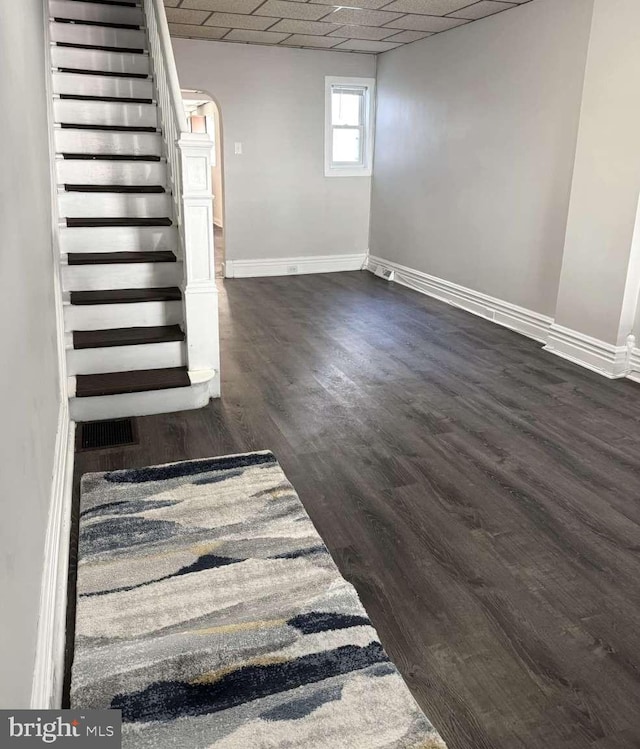 interior space featuring arched walkways, a paneled ceiling, baseboards, stairs, and dark wood finished floors