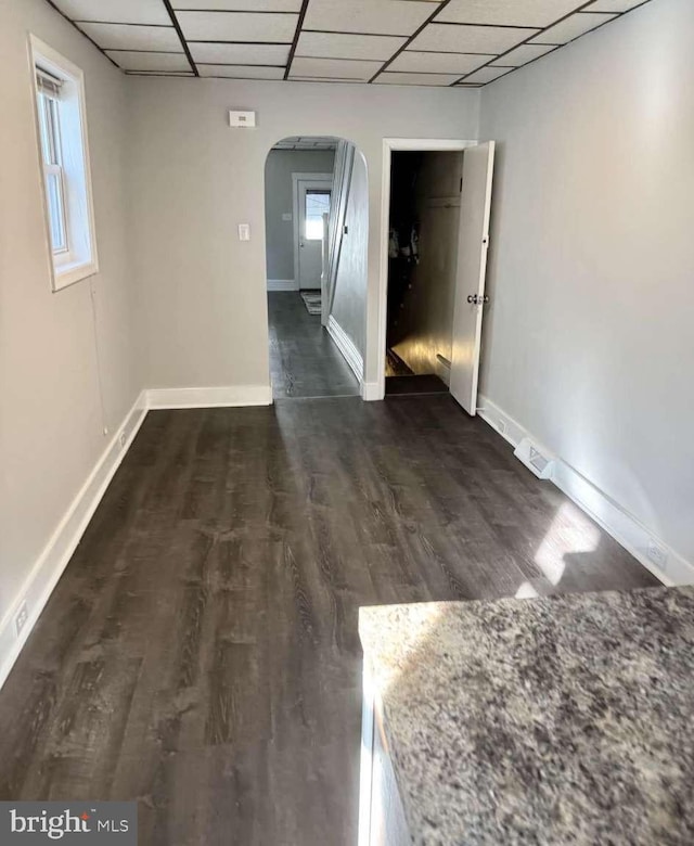 unfurnished room with arched walkways, dark wood-style flooring, a paneled ceiling, and baseboards