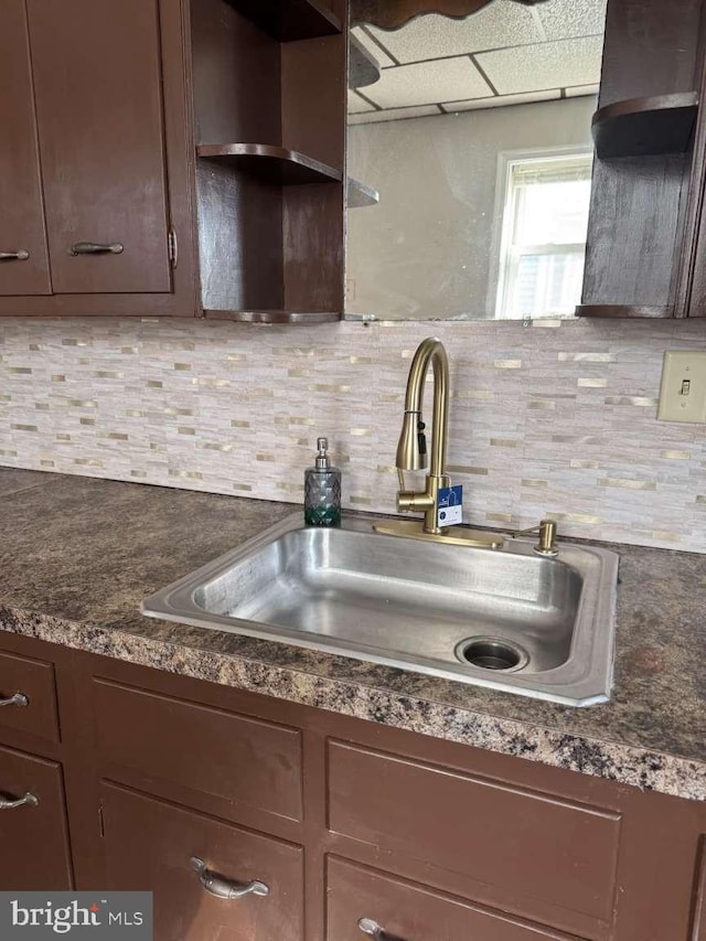 kitchen with dark countertops, tasteful backsplash, dark brown cabinets, and a sink