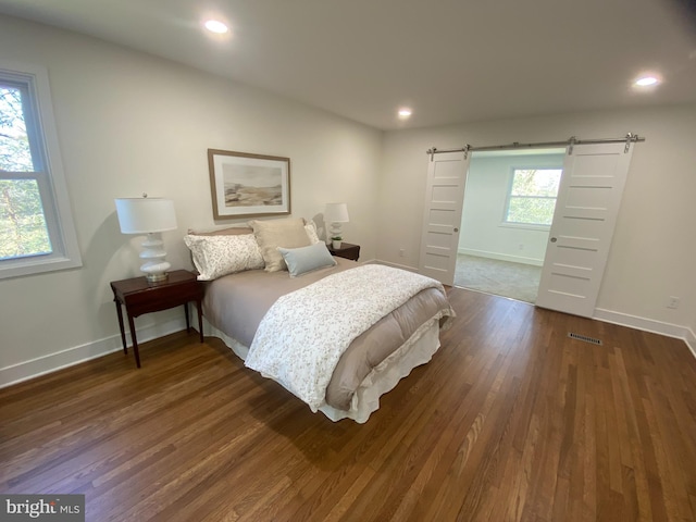 bedroom with a barn door, visible vents, baseboards, dark wood-style floors, and recessed lighting