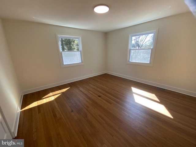 empty room featuring baseboards, visible vents, dark wood-style flooring, and a wealth of natural light